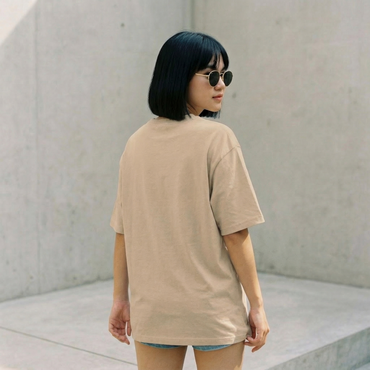 Woman wearing beige oversized t-shirt back view with relaxed fit and minimal aesthetic