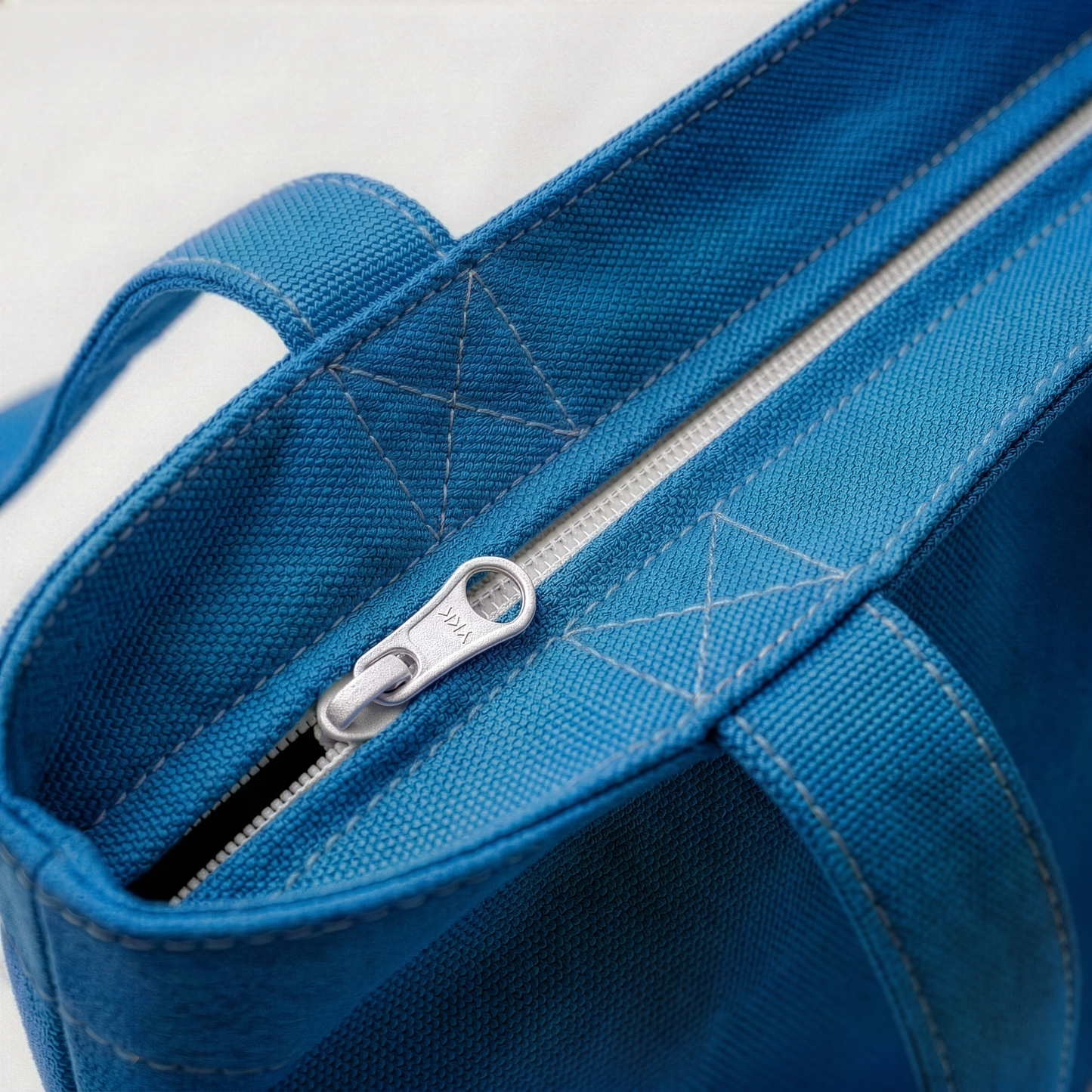 Close up of blue canvas tote bag showing secure black zipper closure and thick stitched handles