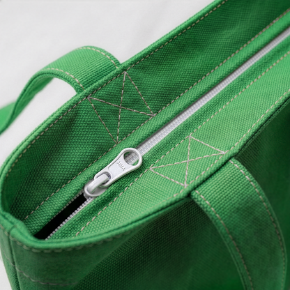 Close-up of green canvas tote bag showing secure zip closure and reinforced stitching on handles