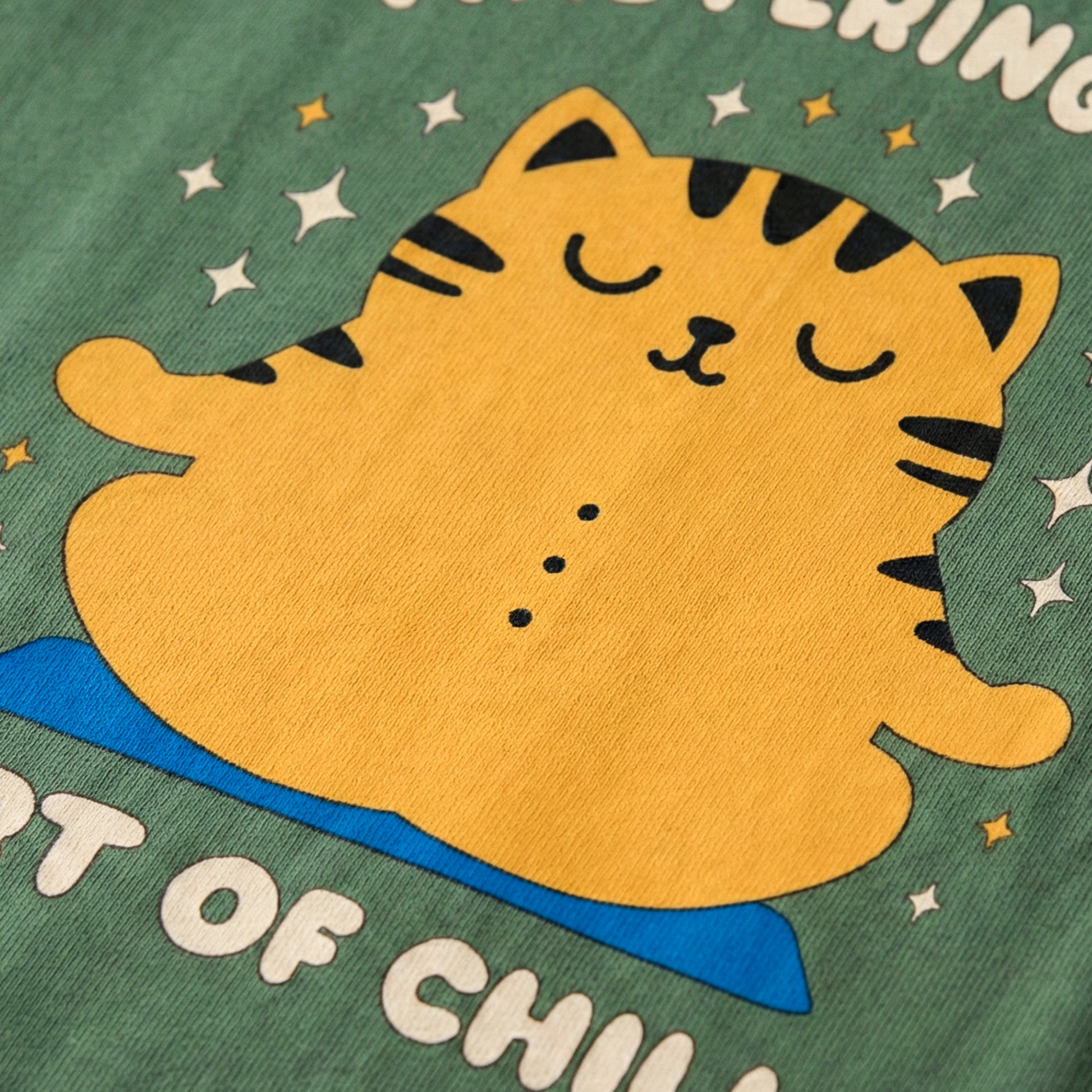 Close-up of yellow meditating cat illustration on green oversized t-shirt