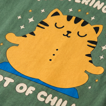 Close-up of yellow meditating cat illustration on green oversized t-shirt