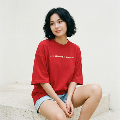Woman sitting wearing red oversized t-shirt overthinking in progress cozy mood